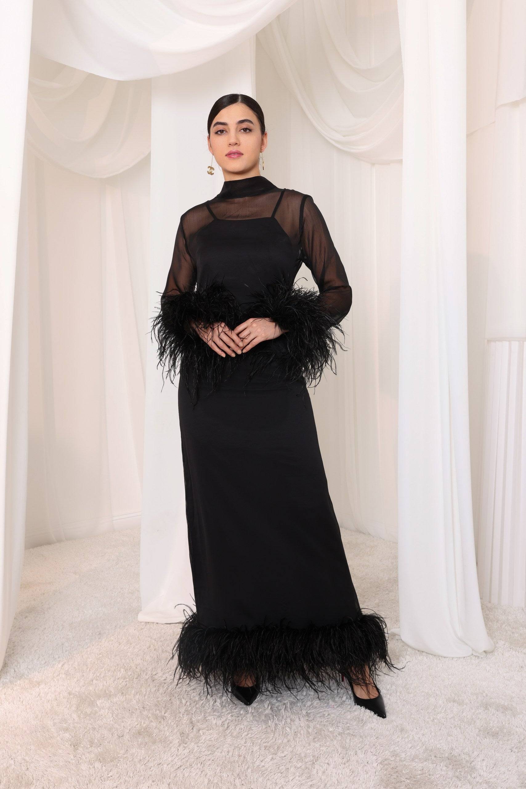 Leila black evening gown with a high neckline and sheer sleeves. Adorned with ostrich feather accents at the cuffs and hem, offering elegant movement.